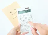給料袋を持ち電卓を使って手取り金額を計算する